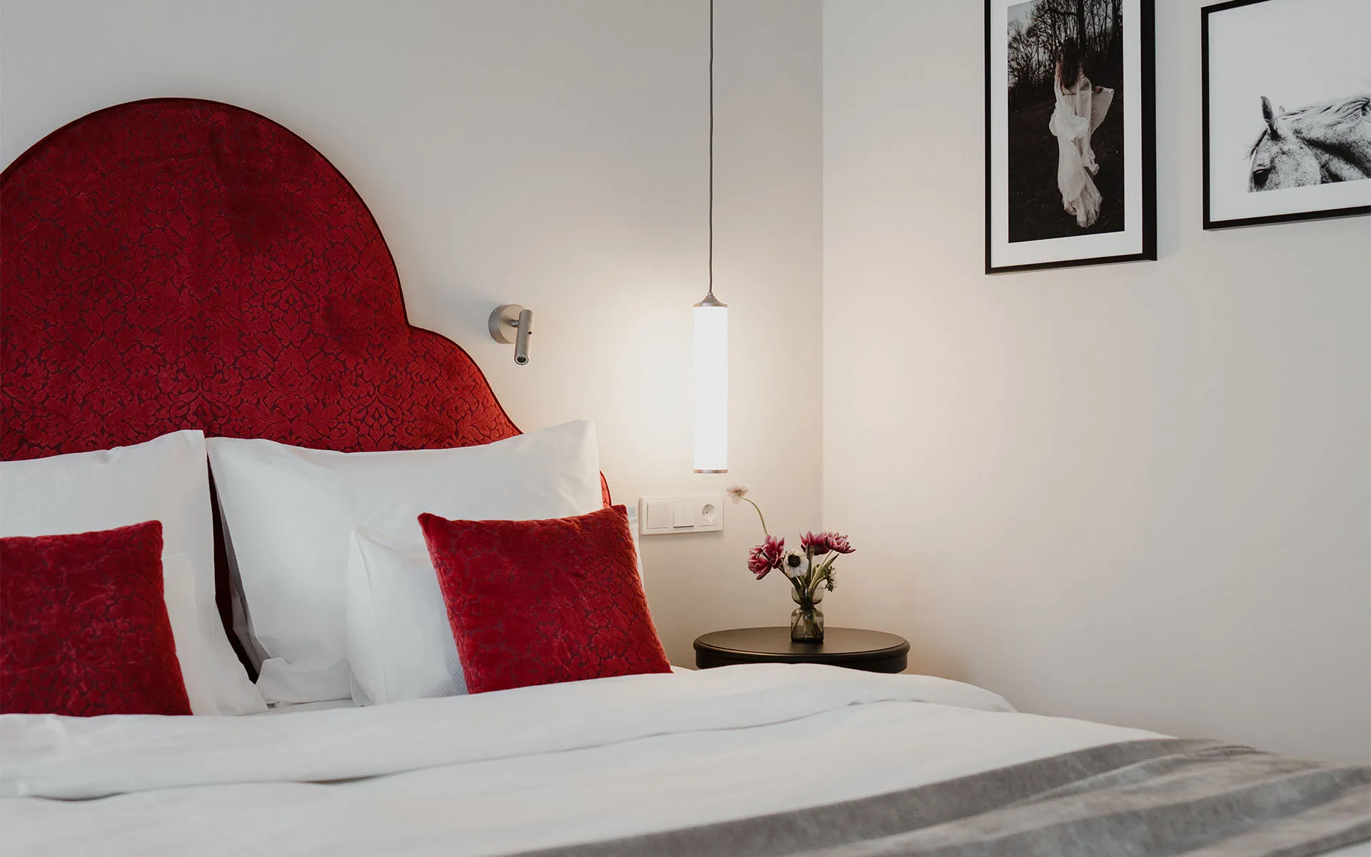 Elegantes Doppelbett mit rotem Samtkopfteil und weißen und roten Kissen im Combi Classic Doppelzimmer mit Balkon im Grand Elisabeth Hotel in Bad Ischl.
