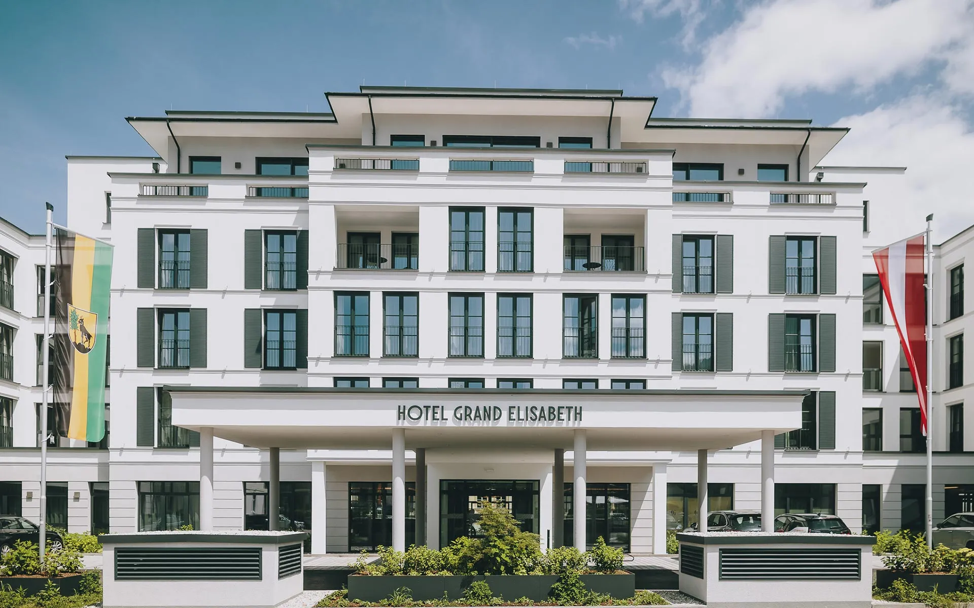 Elegante weiße Fassade des Hotel Grand Elisabeth mit Haupteingang und Fahnen unter blauem Himmel