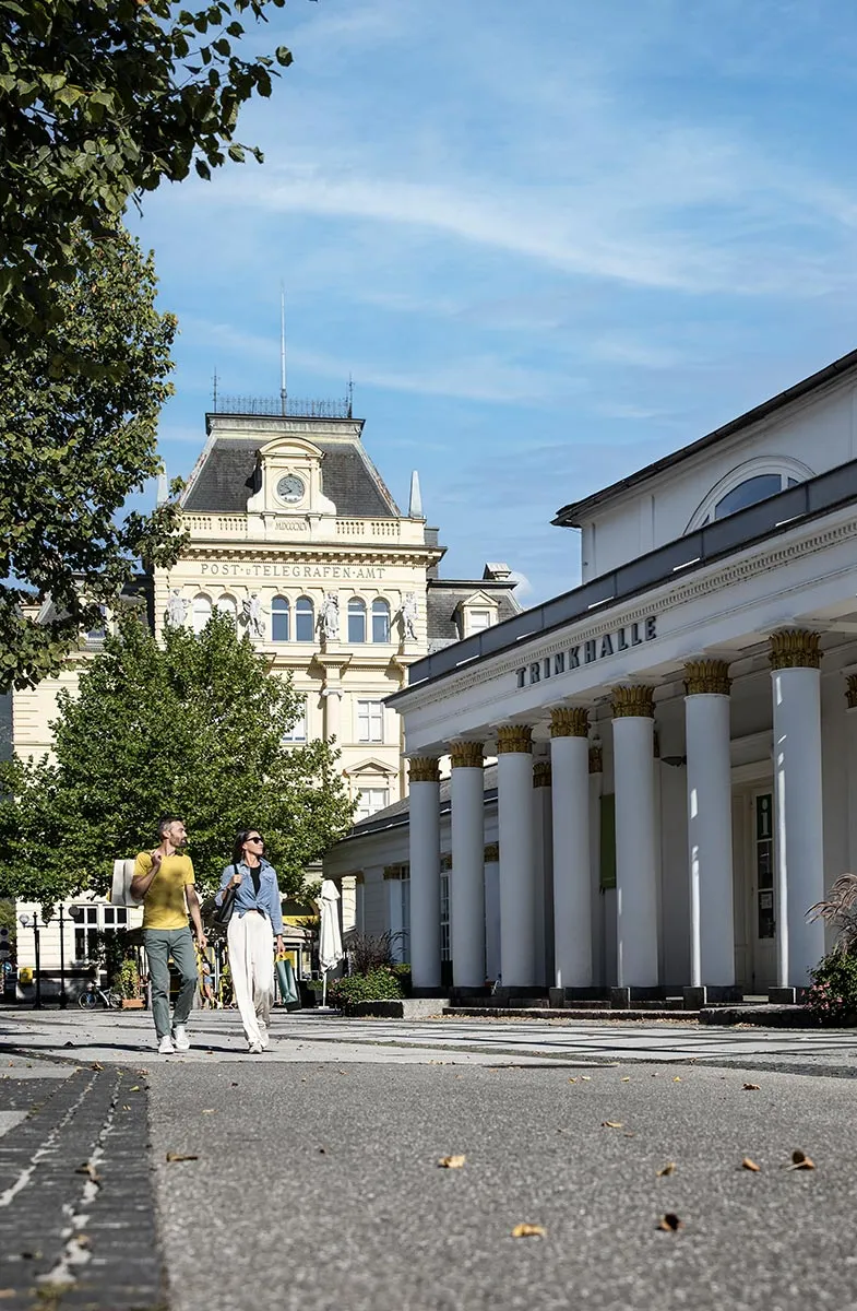 Paar beim Spaziergang vor der historischen Trinkhalle und dem ehemaligen Post- und Telegrafenamt in Bad Ischl