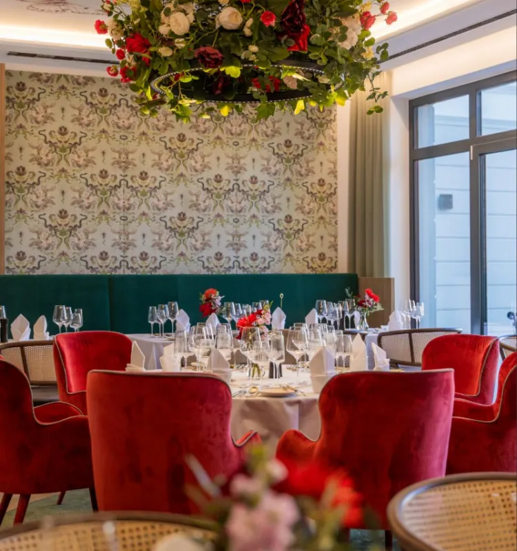 Elegantes Restaurant im Grand Elisabeth Bad Ischl mit roten Samtsesseln, gedeckten Tischen und floralem Kronleuchter