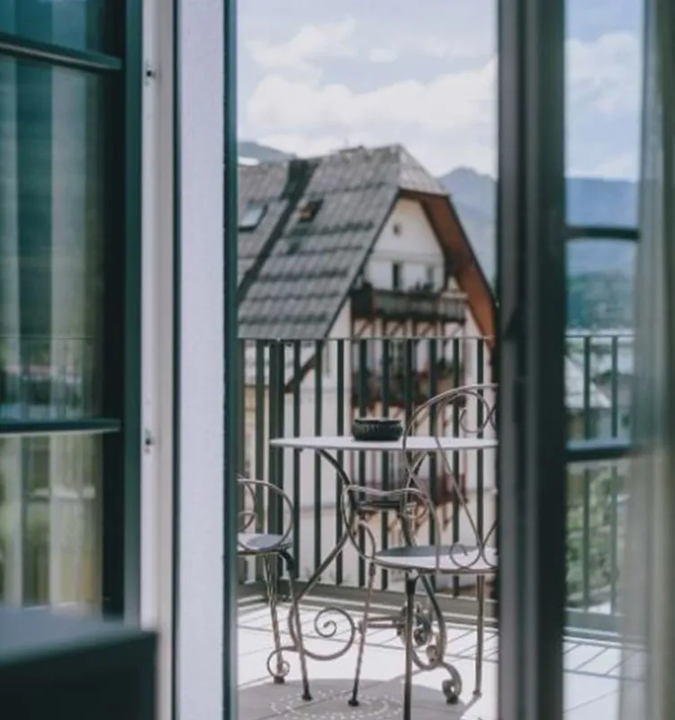 Blick durch die geöffnete Balkontür eines Zimmers im Grand Elisabeth auf Balkon, Dächer und Berge