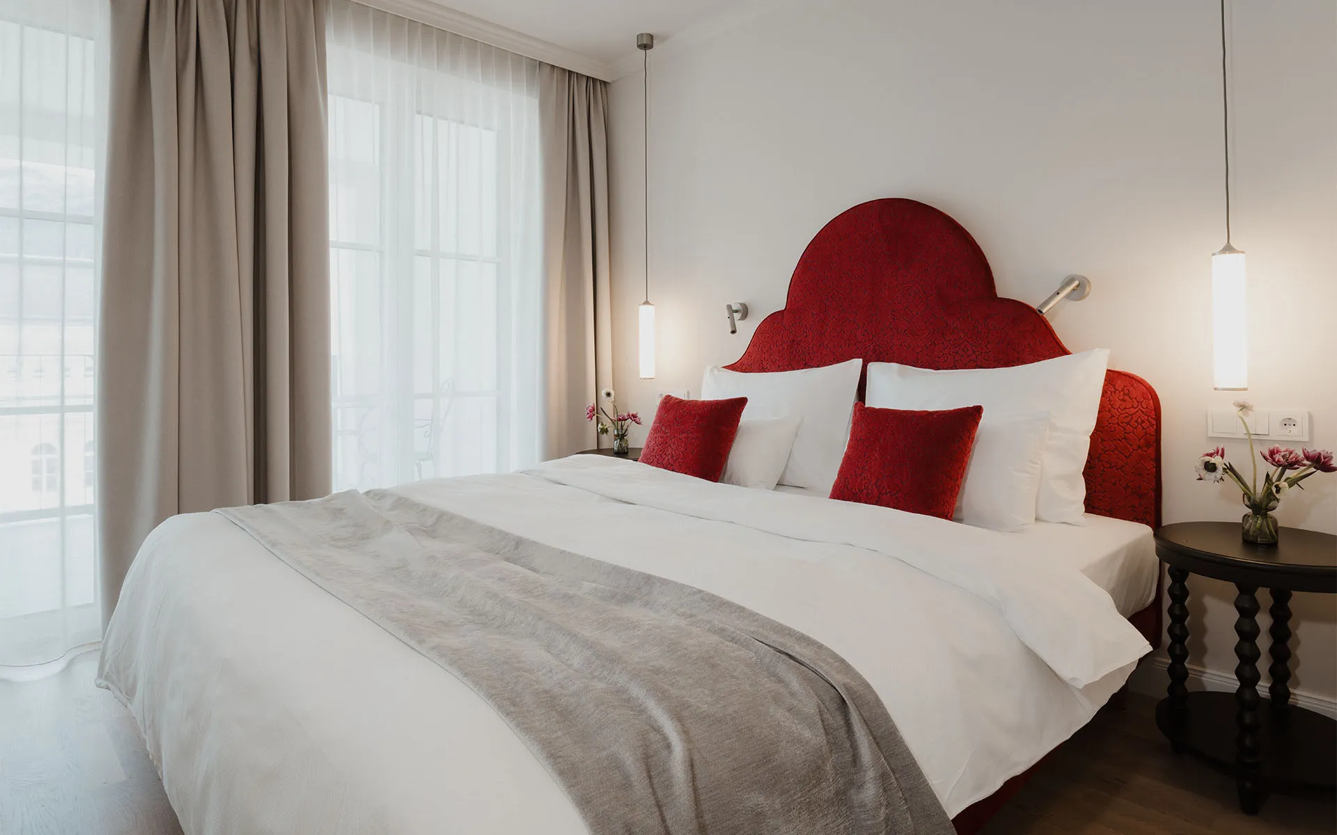 Übersicht des Classic Doppelzimmers mit Balkon mit rotem Kopfteil, weißen Kissen und Balkonzugang im Grand Elisabeth Hotel in Bad Ischl.