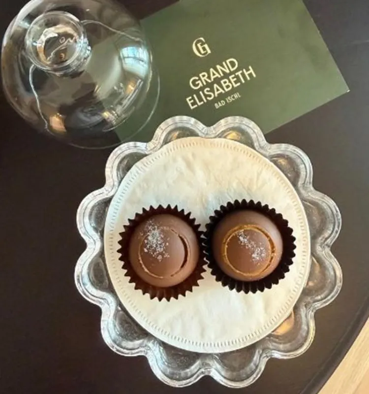 Zwei handgefertigte Pralinen mit Salz auf silbernem Teller neben einer Karte des Grand Elisabeth