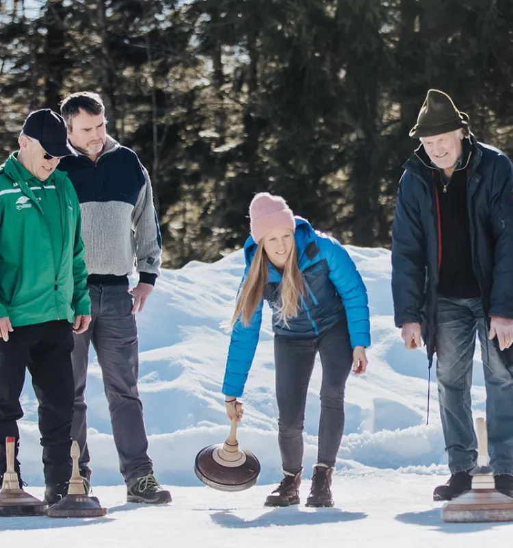 Gruppe beim Eisstockschießen auf einer verschneiten Bahn vor winterlichem Wald