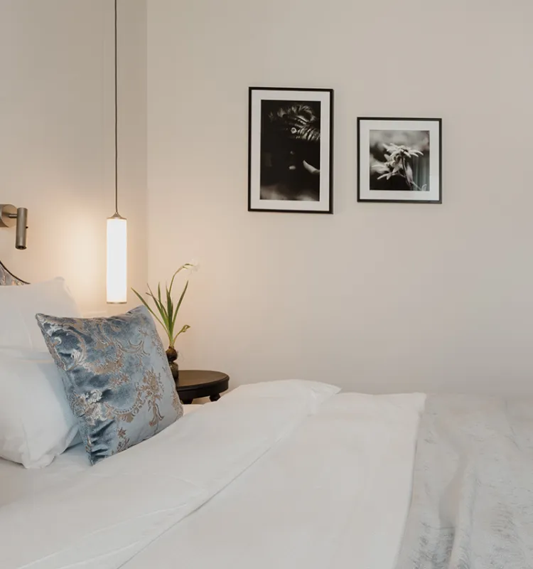 Komfortables Bett mit blauen Kissen, weißen Decken und kunstvollen Bildern an der Wand im Grand Elisabeth in Bad Ischl.