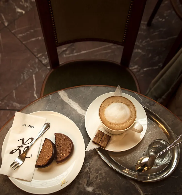 Cappuccino mit Wasser und Schokoladenkuchen auf einem Marmortisch in der Konditorei Zauner.