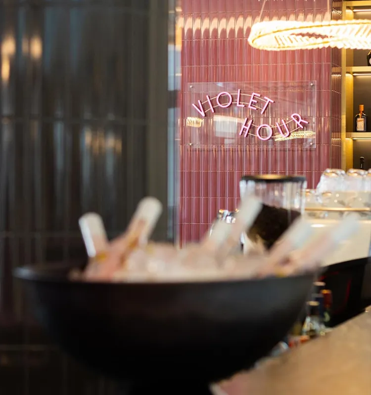 Sektkühler an der Bar Violet Hour im Grand Elisabeth mit rosa Leuchtschrift und warmem Licht