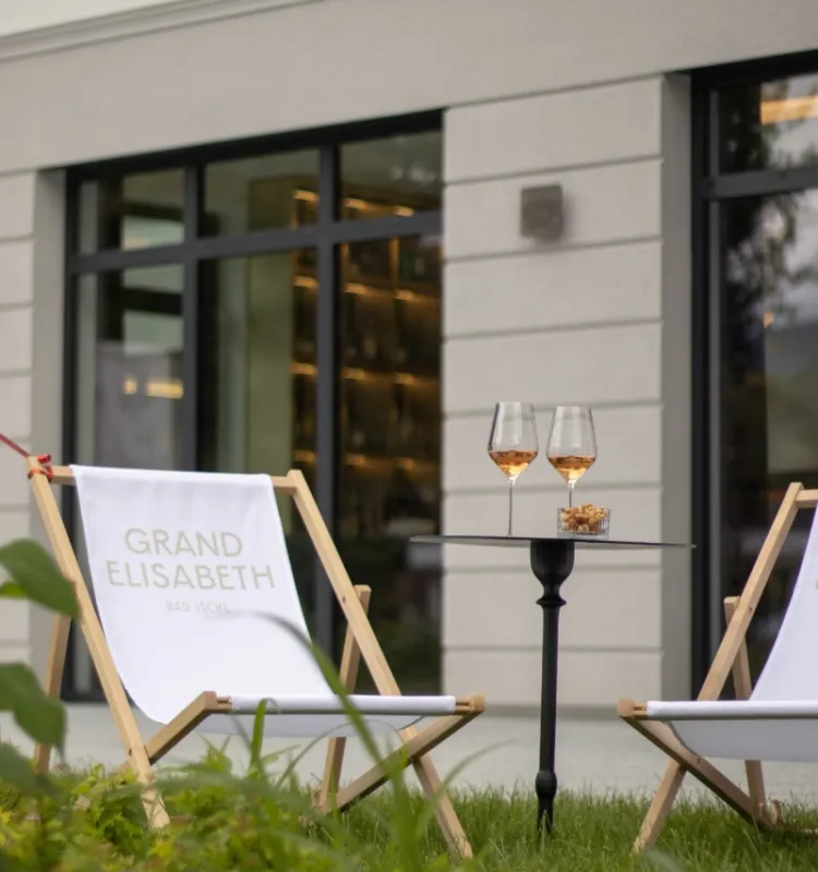Zwei Liegestühle mit Grand Elisabeth Schriftzug im Hotelgarten Bad Ischl, dazwischen ein Tisch mit zwei Gläsern Roséwein