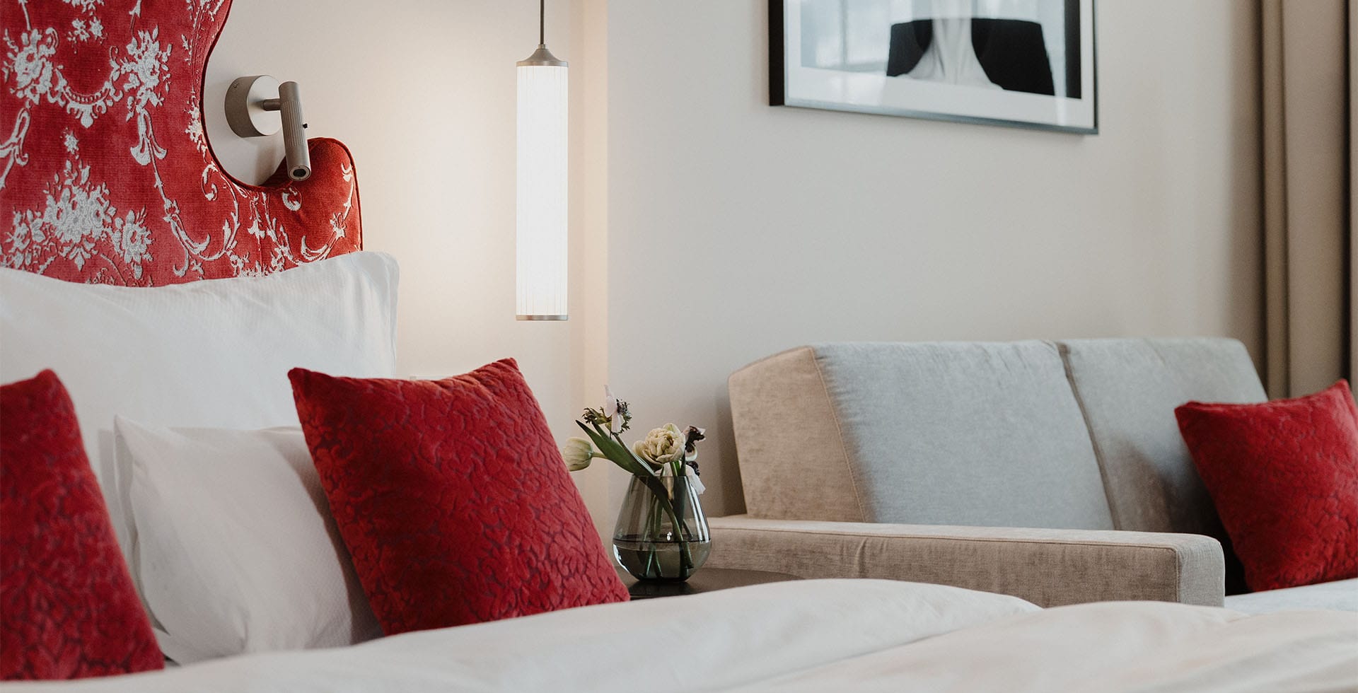 Großzügiges Deluxe Doppelzimmer im Grand Elisabeth Hotel in Bad Ischl mit roten Zierkissen, stilvollem Kopfteil und komfortabler Couch im Hintergrund.