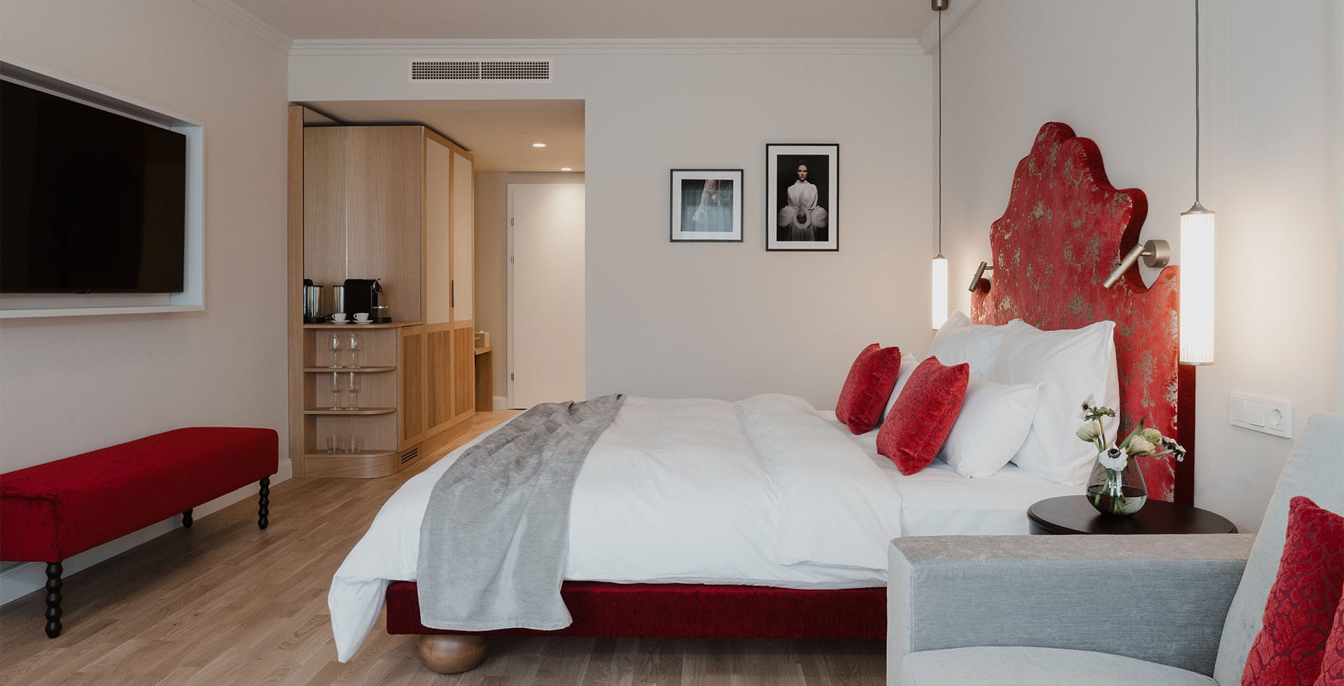 Blick in das Deluxe Doppelzimmer des Grand Elisabeth Hotels mit rotem Kopfteil, weichen Kissen, eleganter Sitzbank und moderner Ausstattung.