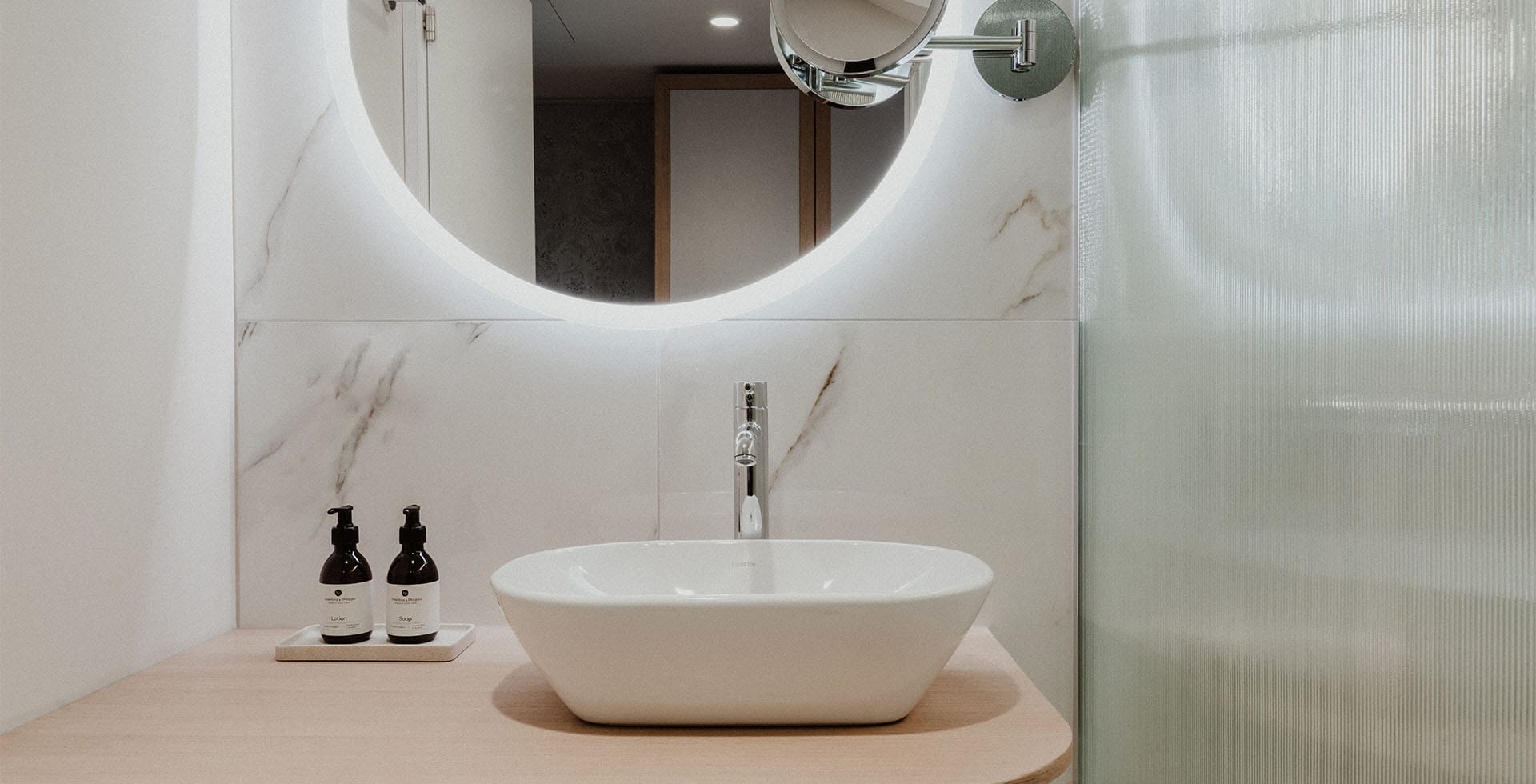 Modernes Bad im Deluxe Doppelzimmer im Grand Elisabeth Hotel mit elegantem Waschtisch, beleuchtetem Spiegel und hochwertigen Pflegeprodukten.