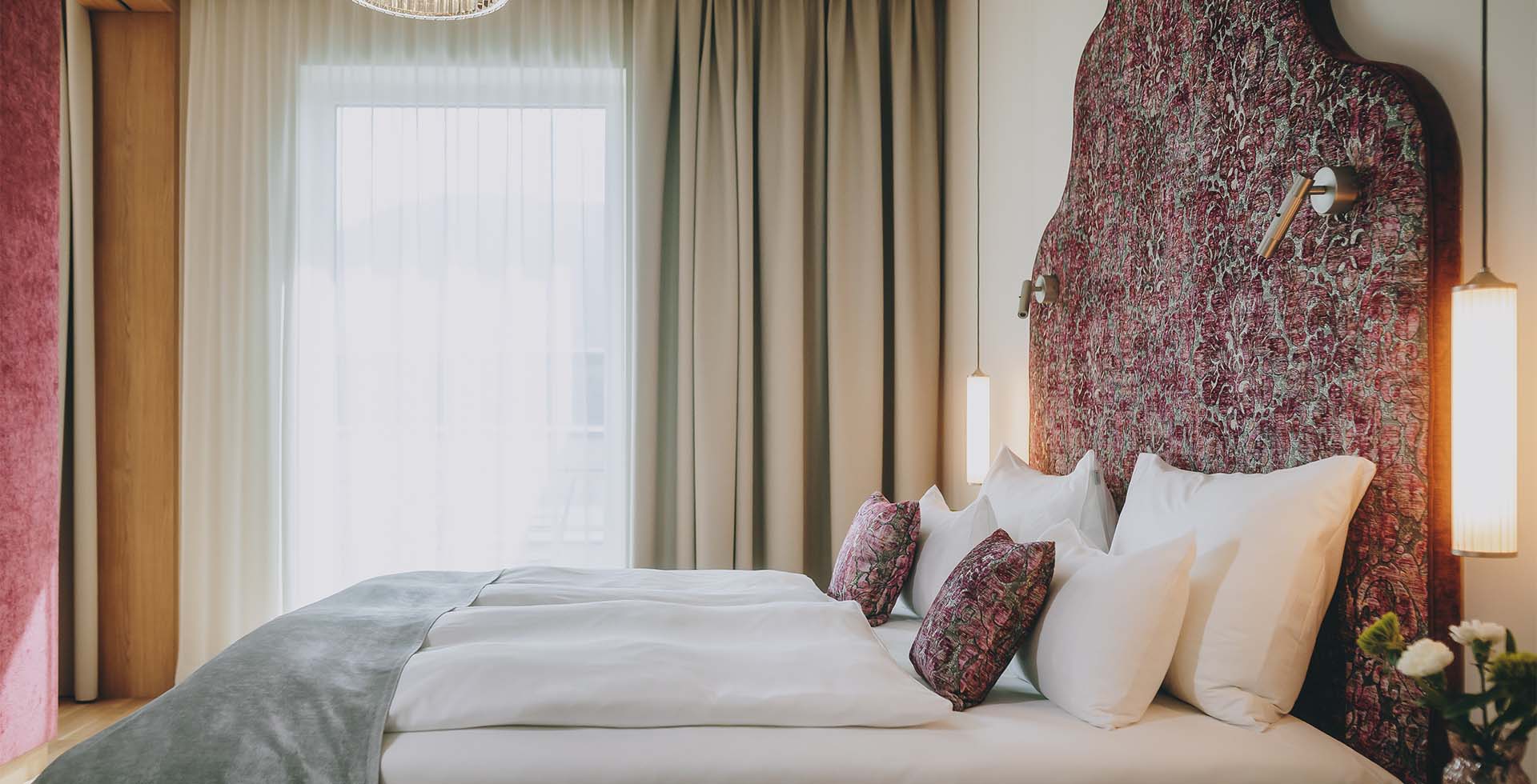 Bett der Kaiser Suite im Grand Elisabeth in Bad Ischl mit dramatischem Stoffdesign, Kissenarrangement und stimmungsvoller Beleuchtung.