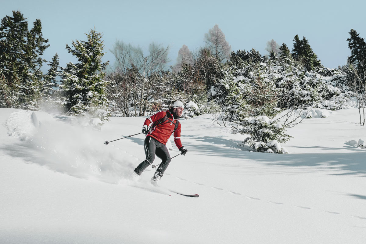 Ein Mann fährt im Winterurlaub im Salzkammergut eine Skipiste hinab, im Hintergrund ragen verschneite Tannen empor.